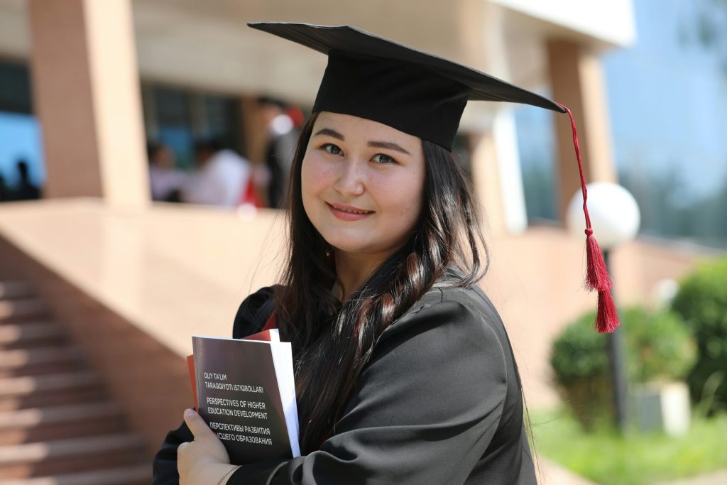 Graduate smiling, holding books in cap.