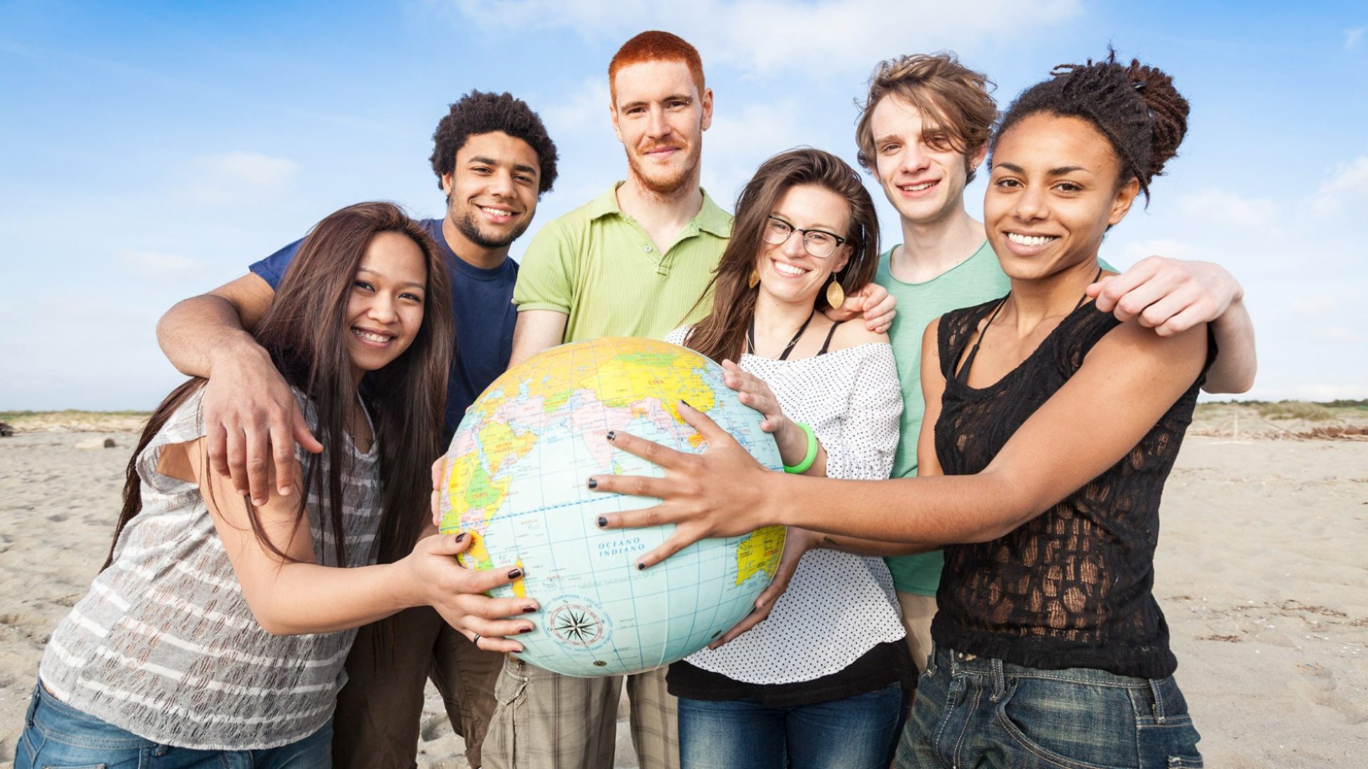 Diverse group holding globe on beach